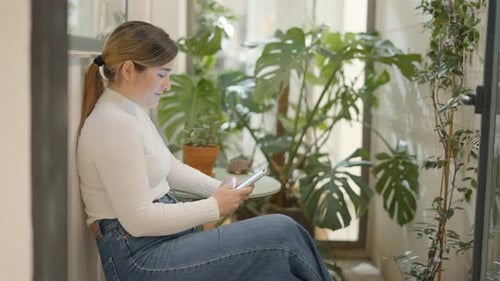 Woman Relaxing with Mobile Phone Surrounded by Plants
