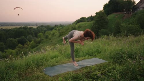 A Young Woman Keeps Her Balance By Doing Yoga Exercises on a Carpet in Nature in the Background a