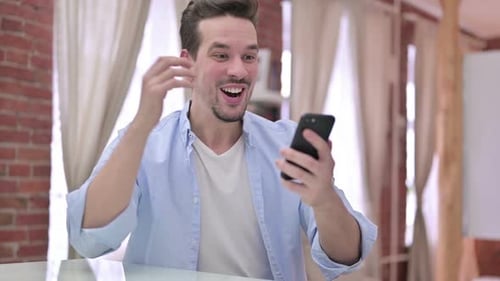 Excited Man Celebrating with Phone Indoors