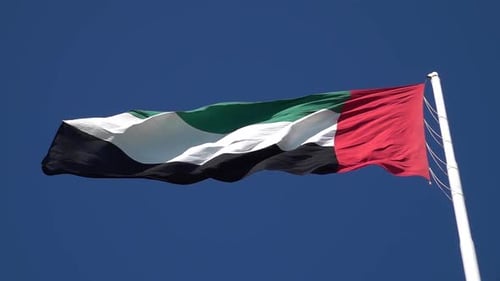 Bandera nacional de los Emiratos Árabes Unidos (EAU) en un mástil ondeando con el viento contra un cielo azul claro
