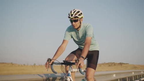 A Man Cyclist in Tight Shorts, a Helmet and Sunglasses Rides on the Side of the Highway, Front View