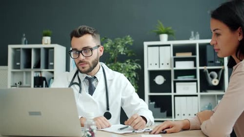 Serious Doctor Talking To Young Woman Patient in Hospital Discussing Disease