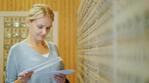 A Middle-aged Woman with Blond Hair Is Standing at the Post Office Next To Individual Cells and
