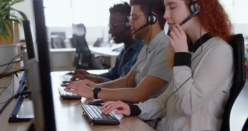 Side view of young cool mixed-race call center team calling and sitting at desk of modern office 4k