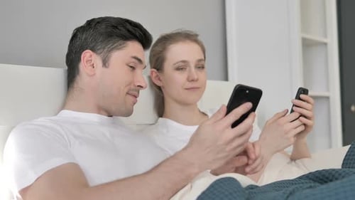 Happy Couple Using Smartphones in Bed
