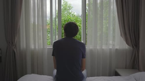 Ein junger Mann in einer obligatorischen Quarantäne. Er sitzt und schaut aus dem Fenster. Er bleibt in einem Zimmer