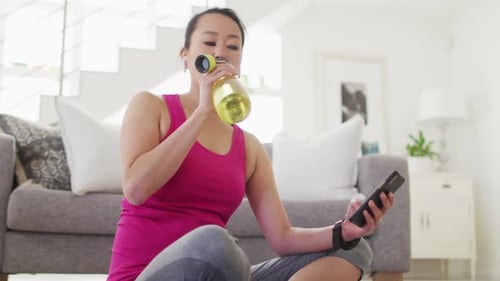 Woman Hydrating and Using Phone After Exercising