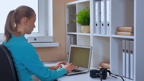 Young Adult Typing at Desk with Laptop and Camera