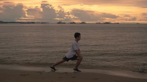 A handsome Asian sportsman stretching exercises before running exercise outside on the beach.