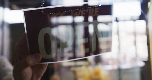Nahaufnahme der Hände einer Cafébesitzerin, die das geschlossene Schild ändert, um es im Fenster zu öffnen