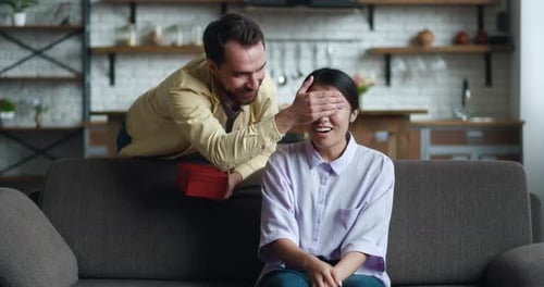 Woman Surprised by Gift from Partner on Sofa
