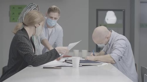 Group of Young Colleagues in Covid Face Masks Sitting at the Table in Office and Talking