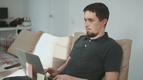 Man Sitting on Couch Uses Laptop at Home