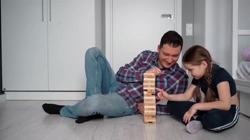 Father and daughter. They play tower and laugh. They sometimes look at the camera. Positive emotions