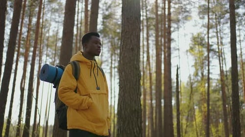 African Black Man Climbs Uphill in Woods in Yellow Jacket with Backpack in Slow Motion