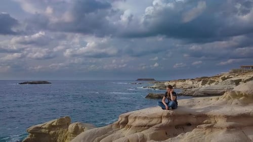 A Girl Sits on a Rock on the Sea Coast