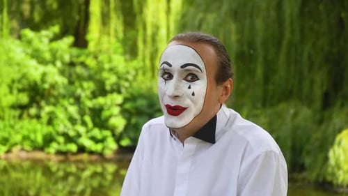 Lustiger Pantomime, der in die Kamera schaut und auf grünem Hintergrund in einem Park lächelt. Gefühl der Freude