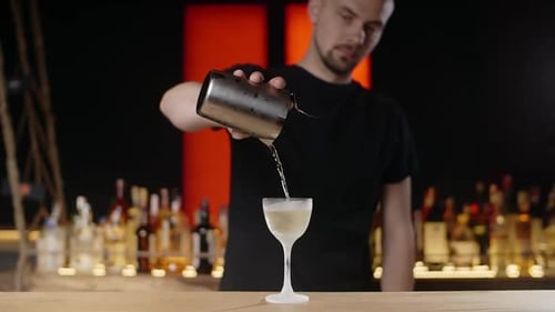 Bartender Pouring Cocktail into Stemmed Glass in Bar