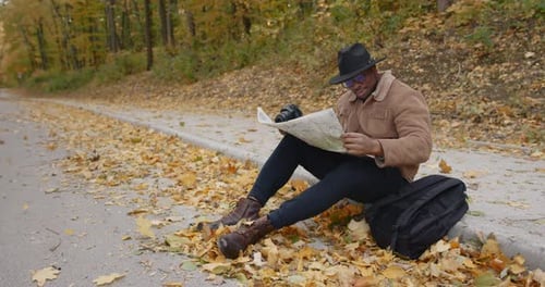 A Black Traveler Sits on the Roadside with a Map
