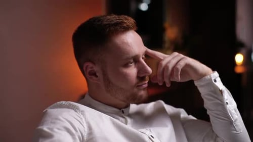 Close-up of Face of Thoughtful Handsome Young Bearded Man Sitting in Soft Armchair at Home.