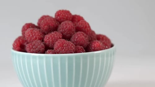 Reife Himbeeren in einer Schüssel rotieren auf hellem Hintergrund