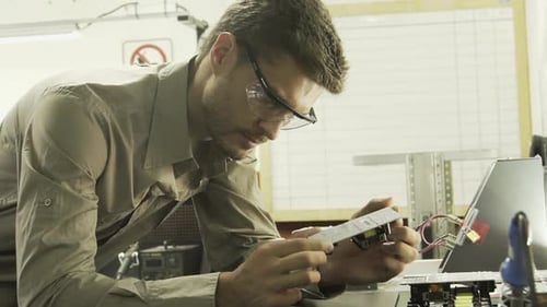 Elektroingenieur untersucht Leiterplatte und lächelt dann in die Kamera