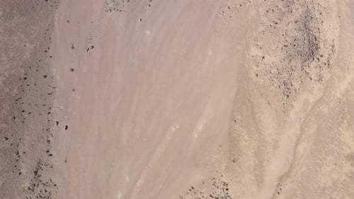 Flying over a barren landscape of brown grey sand and rock formations with many craters