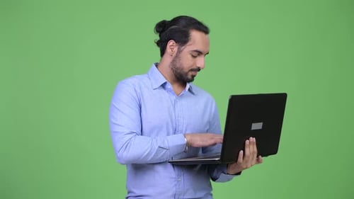 Profile View of Young Happy Bearded Indian Businessman Using Laptop
