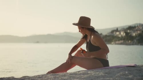 Girl Applies Sun Protection Cream on the Body on the Beach Near the Ocean