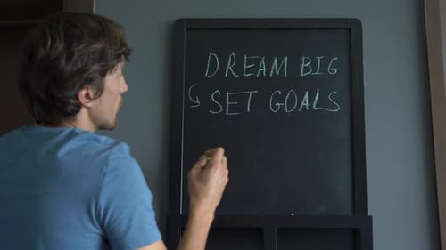 Nahaufnahme eines jungen Mannes, der eine Botschaft „Dream Big, Ziele setzen, Maßnahmen ergreifen“ auf einem zeichnet