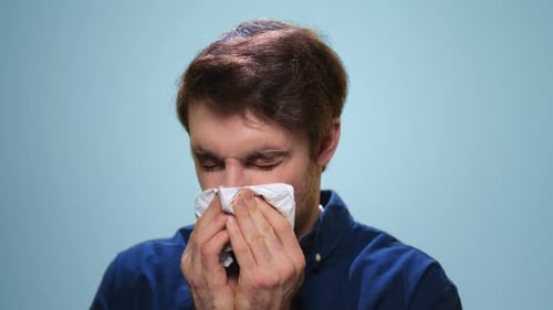 Sick Man Sneezing in Studio. Ill Man Using Napkin on Blue Background