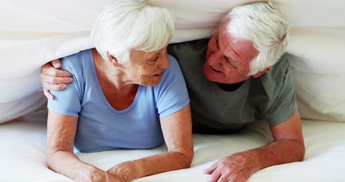 Senior Couple Laughing Together on White Bed