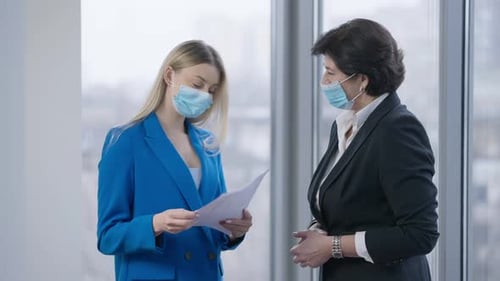 Businesswomen Discussing Documents in Modern Office Wearing Masks