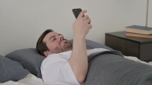 Man Relaxing in Bed with Mobile Phone