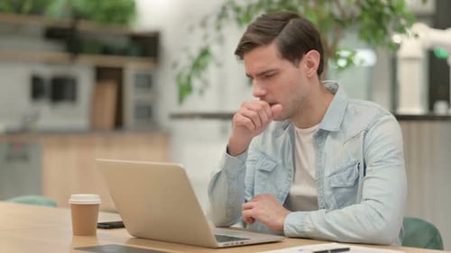 Young Adult Coughing While Working on Laptop
