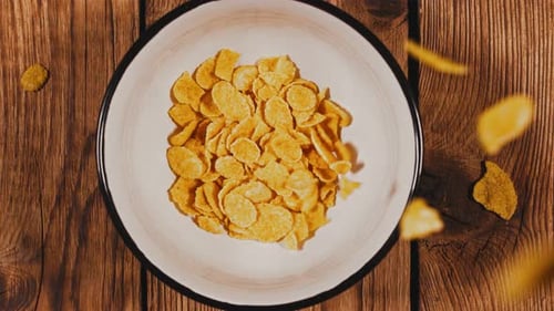 Golden Cornflakes Falling into Bowl on Wooden Table