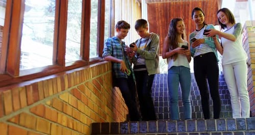 Group of smiling school friends using mobile phone in corridor
