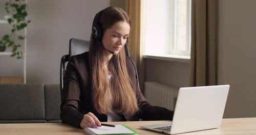 Young Business Woman in Strict Black Suit Sits in Office at Table Uses Laptop To Work Remotely