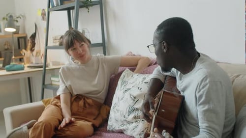 Woman Listening to Man Playing Guitar on Sofa