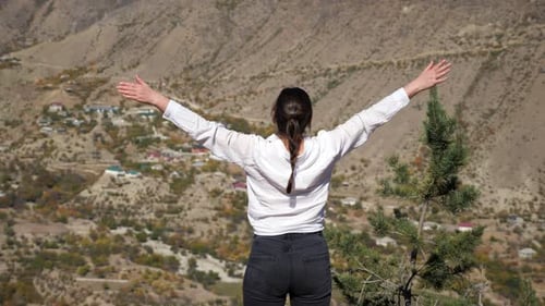 Young Woman in White Shirt Enjoying the View of the Valley with Her Arms Spread Rear View