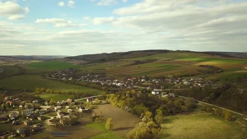 Aerial view of countryside village with small houses among green trees with farm fields