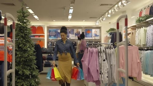 Happy African American Woman with Paper Bags Walks Out of Women's Clothing Store in Mall