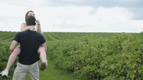 Man Lifts Woman in Field and Kisses Her