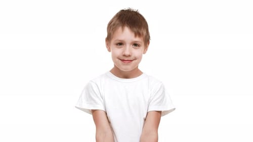 Verlegener Junge im Grundschulalter, der auf weißem Hintergrund steht und lächelt und zeigt die Zunge