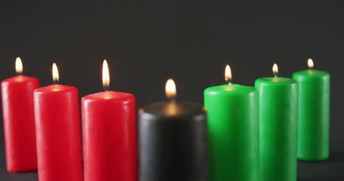 Composition of halloween green, black and red lit candles against black background