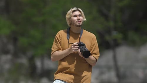 Young Man Photographer Takes Photos of Nature on His Camera in the Forest