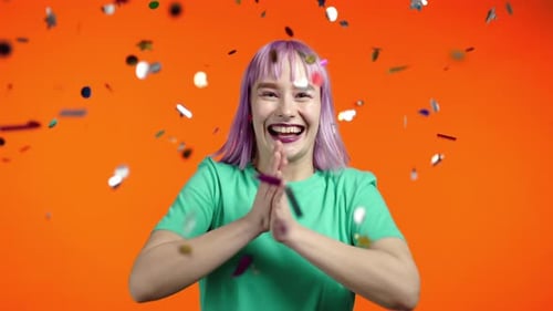 Cheerful Woman Celebrates with Confetti on Orange Background