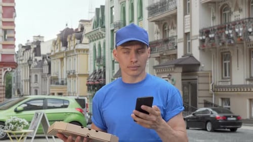 Male Courier Delivering Pizza in the City Calling Is Client on the Phone