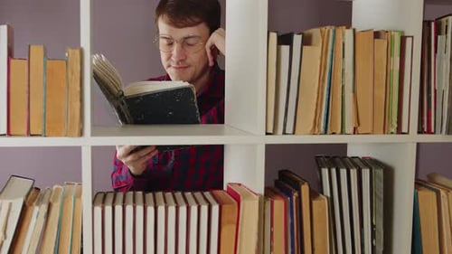 Libro de lectura de hombre con gafas de pie detrás de la estantería