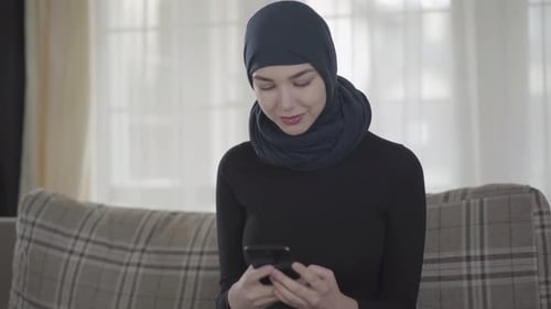 Portrait d'une jeune femme musulmane indépendante tapant un message à l'aide d'un smartphone